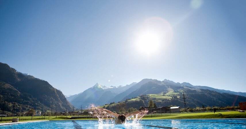 Schwimmer im Sportbecken vor Bergpanorama unter strahlendem Himmel