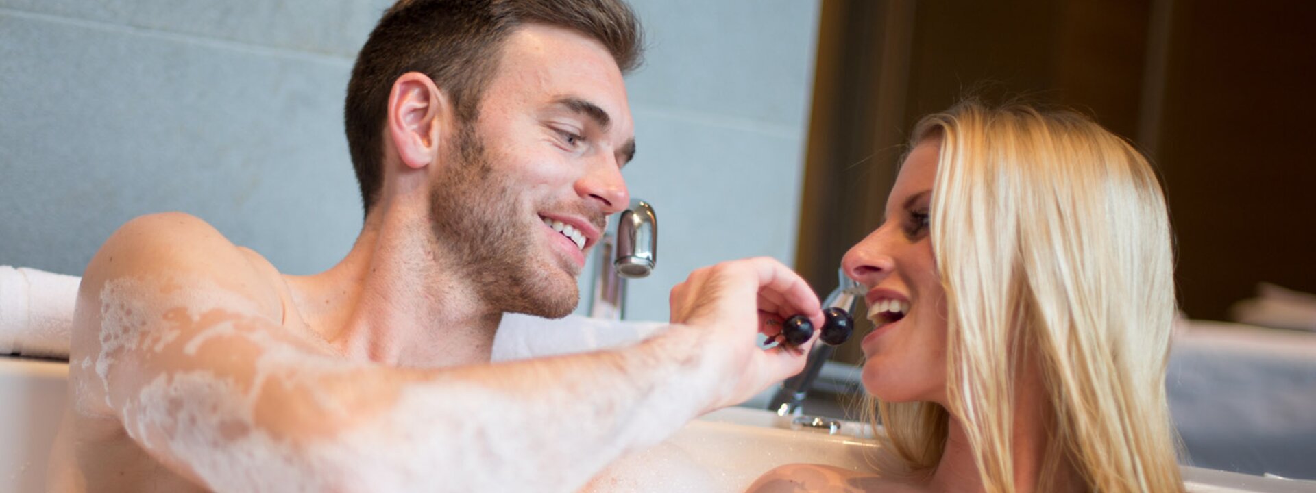 Paar in Badewanne mit Schaum, Mann füttert Frau mit Trauben