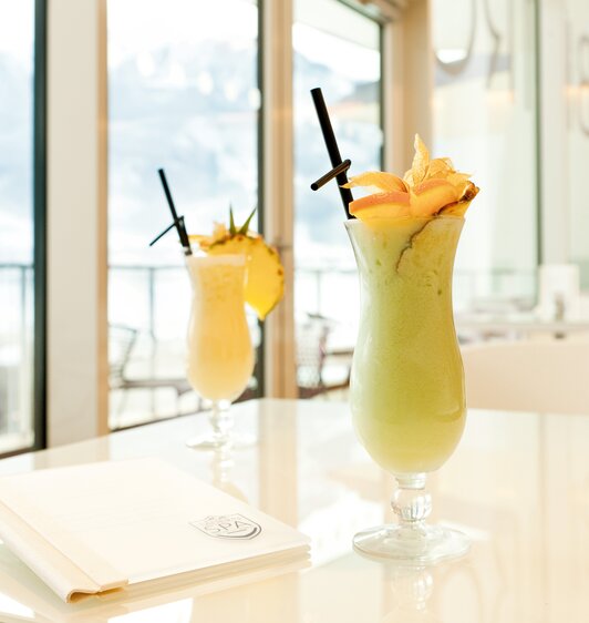 Zwei Cocktails mit Ananasgarnitur auf einem Tisch vor einem Fenster
