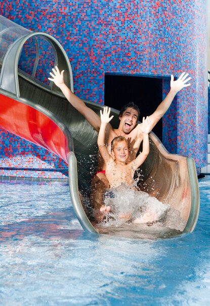 Vater und Kind rutschen lachend eine Wasserrutsche in ein Schwimmbad