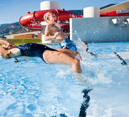 Children splashing outdoors in a swimming pool in front of a red water slide