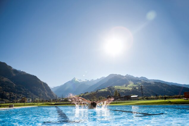 Schwimmer im Sportbecken vor Bergpanorama unter strahlendem Himmel