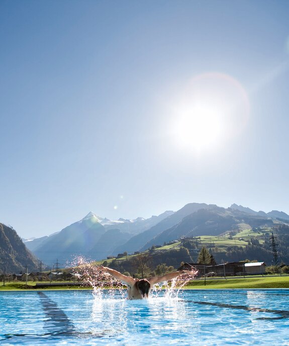 Swimmers in the sports pool in front of a mountain panorama under a bright sky