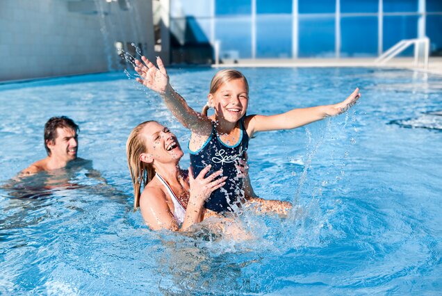 Mother holding laughing girl in swimming pool, splashing water