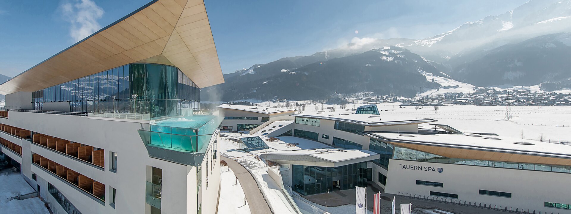 Hotelanlage im Winter mit Pool auf dem Dach und schneebedeckten Bergen im Hintergrund