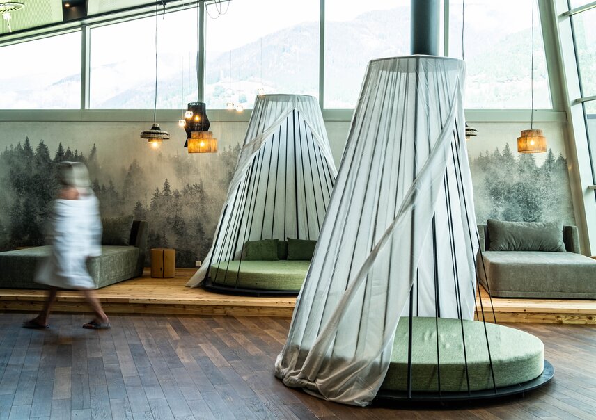Two conical beds with curtains in a room with wooden floors and forest wallpaper
