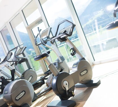 Fitnessraum mit Trainingsgeräten vor Panoramafenster mit Bergblick