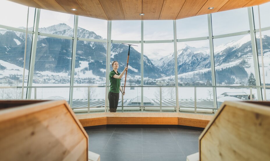 Frau putzt Fenster mit Eiskratzer vor Bergpanorama