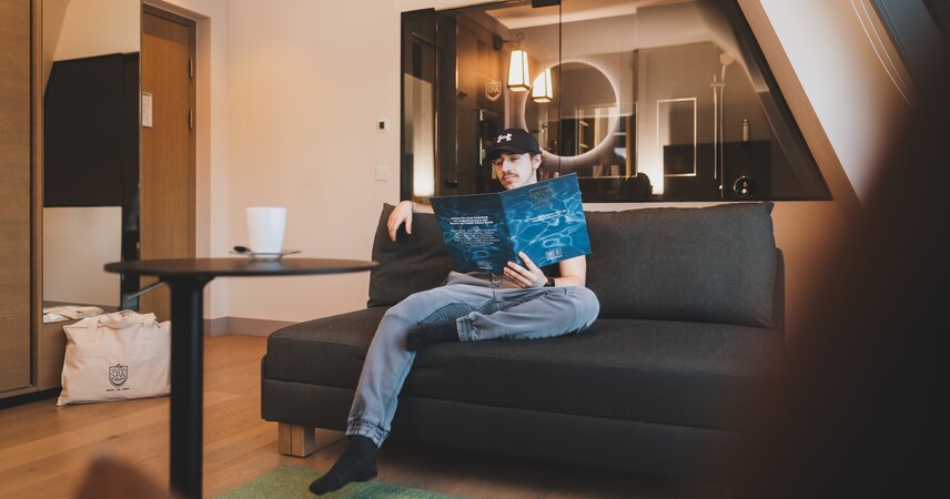 Junger Mann liest Broschüre auf Sofa im Hotelzimmer