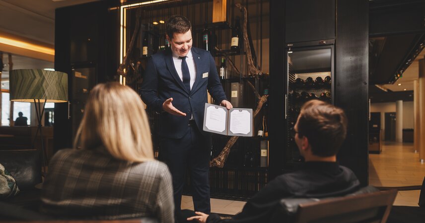 Sommelier berät Gäste mit Weinkarte im Hotel