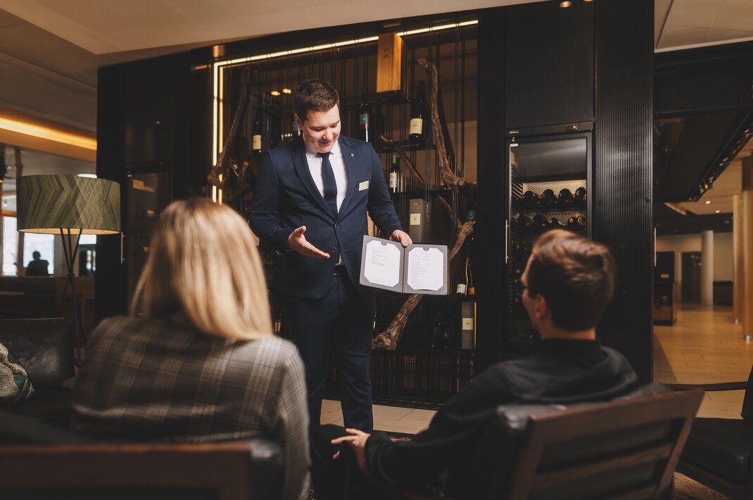 Sommelier berät Gäste mit Weinkarte im Hotel