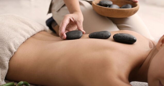 Hot stone massage on the back with dark stones and hands of a masseuse | © africa-studio.com (Olga Yastremska and Leonid Yastremskiy)