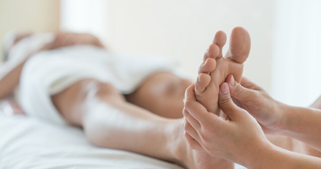 Foot reflexology massage: Hands massage a foot on a white couch | © lOvE lOvE