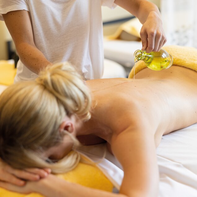 Woman lying on her stomach while masseuse pours oil on her back