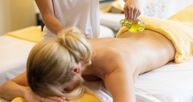 Woman lying on her stomach while masseuse pours oil on her back