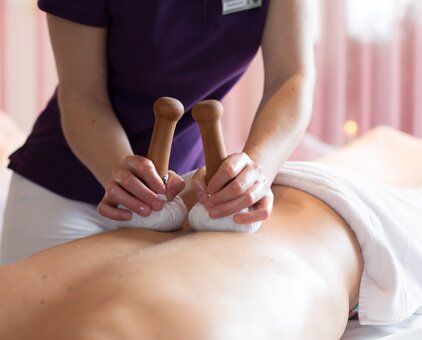 Herbal stamp massage on the back with two stamps in the hands of the masseuse