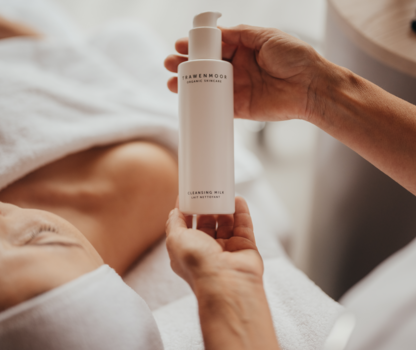 Hands holding cleansing milk bottle from Trawenmoor over a person lying down