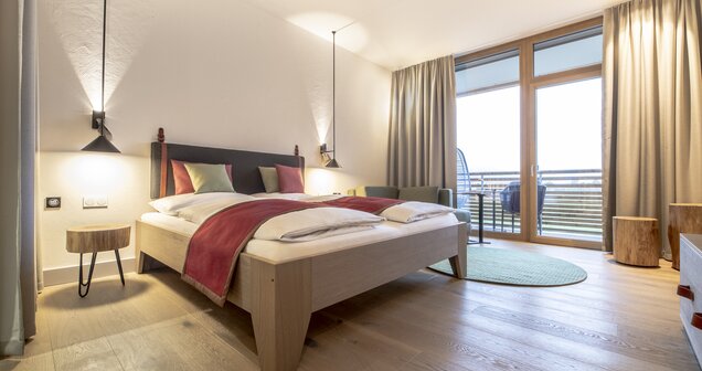 Bright double room with wooden floor, large bed, balcony and nature view