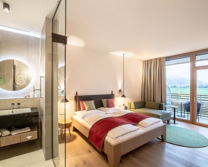 Doppelzimmer mit Doppelbett, Sitzecke und Blick durch ein Fenster