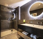 Modern bathroom with shower, vanity unit and round mirror with lighting